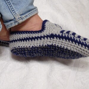May include: Close-up of a pair of crocheted slippers with a gray and blue striped pattern. The slippers are worn on a person's feet.