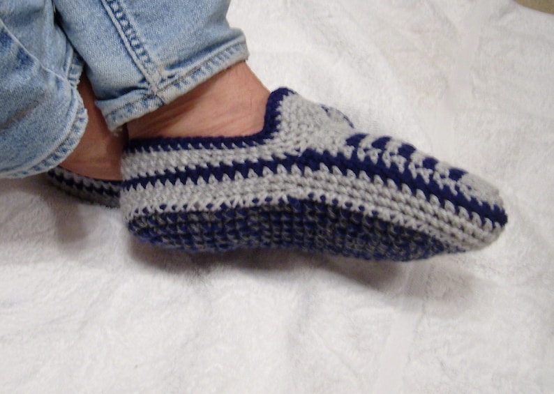 May include: Close-up of a pair of crocheted slippers with a gray and blue striped pattern. The slippers are worn on a person's feet.