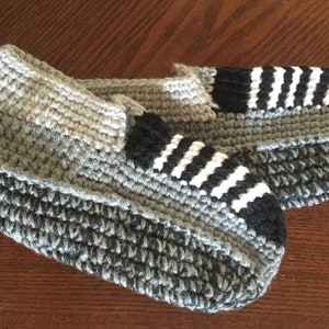 May include: A pair of gray, black, and white crocheted slippers. The slippers have a striped pattern on the top and a solid gray bottom.
