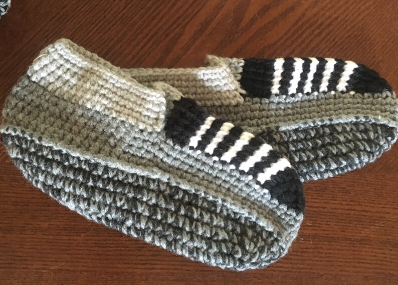 May include: A pair of gray, black, and white crocheted slippers. The slippers have a striped pattern on the top and a solid gray bottom.