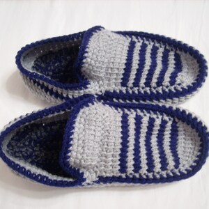 May include: A pair of gray and blue striped knitted slippers with a blue crocheted trim.