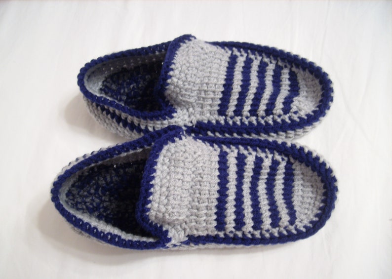 May include: A pair of gray and blue striped knitted slippers with a blue crocheted trim.