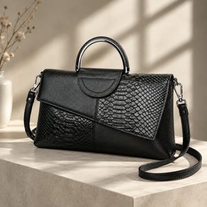 Può includere: Una borsa a mano nera che combina pelle granulata e un pannello testurizzato con motivo a pelle di serpente. La borsa include un manico superiore semicircolare in metallo argentato, una chiusura a patta e una tracolla nera rimovibile e regolabile.