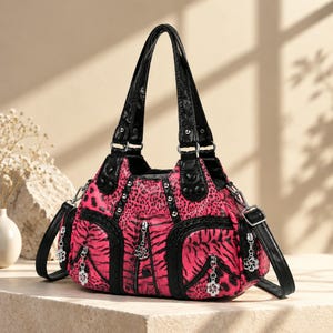 May include: A handbag featuring a vibrant hot pink and black animal print pattern with black leather-like trim. The bag includes multiple exterior zippered pockets, silver-toned metal studs, and decorative flower-shaped zipper pulls.