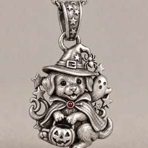 Puede incluir: Un colgante de tono plateado que muestra un cachorro con un sombrero de bruja y una capa con una pequeña piedra roja en el cuello. El cachorro sostiene un cubo de calabaza, acompañado por un fantasma y estrellas. El colgante cuelga de una cadena.