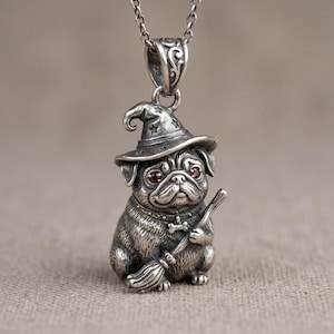 Pode incluir: Um pingente de prata esterlina em uma corrente apresentando um cão pug detalhado usando um chapéu pontudo com recortes de estrelas e segurando uma vassoura. O pug tem pequenos olhos de pedra vermelha e uma coleira com uma etiqueta de osso.
