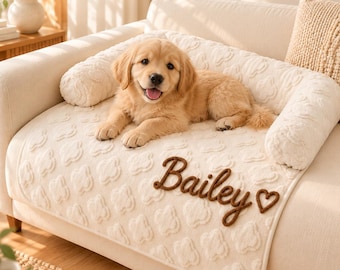 Può includere: Una cuccia per animali color crema con bordi laterali rialzati e un motivo a nuvole testurizzato. La cuccia presenta il nome Bailey ricamato in corsivo marrone, seguito da un piccolo simbolo a forma di cuore marrone, con un cucciolo di golden retriever.