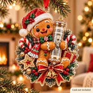 May include: A gingerbread person Christmas ornament wearing a red Santa hat and a plaid scarf, holding a clear cylindrical tube containing a one hundred dollar bill. The ornament is decorated with candy canes, a star cookie, and a red bow.