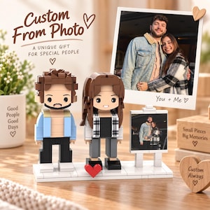 May include: A custom building block set featuring two figures, one with brown hair and a blue jacket, the other with long brown hair and a plaid shirt, standing on a white base next to a small framed photo and a larger photo print labeled You + Me.