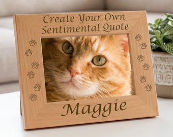 May include: A light-coloured wooden picture frame featuring engraved paw prints along the sides. The top border displays the text "Create Your Own Sentimental Quote" and the bottom border features the name "Maggie" in a cursive font.