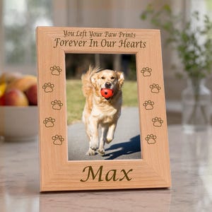 May include: A light-colored wooden picture frame featuring the engraved text "You Left Your Paw Prints Forever In Our Hearts" at the top, the name "Max" at the bottom, and paw print icons along the sides, holding a photo of a dog.