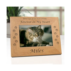 May include: A light brown wooden picture frame featuring the engraved text You Left Your Paw Prints Forever In My Heart at the top and the name Miles at the bottom, with small paw print designs engraved along the left and right vertical borders.