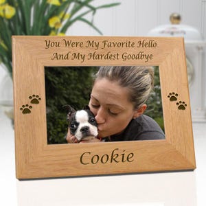 May include: A rectangular light brown wooden picture frame featuring the engraved text "You Were My Favorite Hello And My Hardest Goodbye" at the top and "Cookie" at the bottom, with two small paw print cutouts on both the left and right sides.
