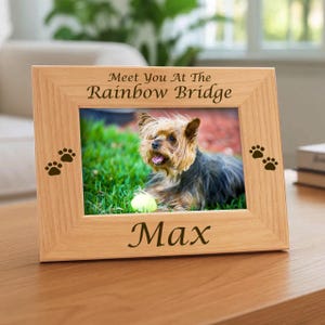 May include: A light-colored wooden picture frame featuring the engraved text Meet You At The Rainbow Bridge at the top and the name Max at the bottom. Two small paw print icons are engraved on both the left and right sides of the frame.