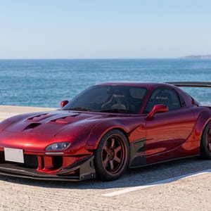 May include: A metallic dark red sports car featuring a wide body kit, a large rear wing, and dark-colored multi-spoke wheels. The vehicle has a vented hood, a front splitter, and tinted windows. The text NijionE is visible in the bottom right corner.