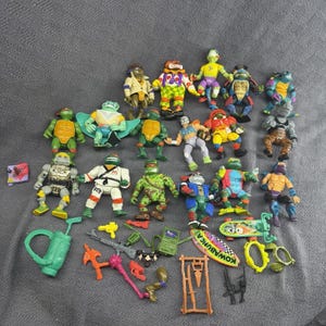 Puede incluir: Una colección de figuras de acción y accesorios de Teenage Mutant Ninja Turtles, que incluye varios personajes con trajes coloridos, armas de plástico, una mochila verde, una tabla de surf con el texto Kowabunga y una pequeña tarjeta cuadrada.