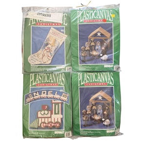 May include: Four Bernat plastic canvas Christmas craft kits in original packaging. Includes a stocking pattern, a train design with the word NOEL, and two identical nativity scene sets featuring figures and a stable structure.