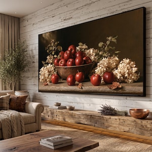 Op de afbeelding: Een grote rechthoekige wandkunstprint met een stilleven van felrode appels in een donkere houten kom, omringd door trossen gedroogde beige hortensiabloemen op een rustiek stenen oppervlak tegen een donkere achtergrond.