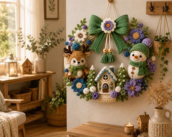 May include: A decorative crochet wreath featuring a central house, a reindeer, and a snowman. The wreath is adorned with green, purple, and white flowers, green pine trees, and a large green bow at the top with a white flower centre and tassels.