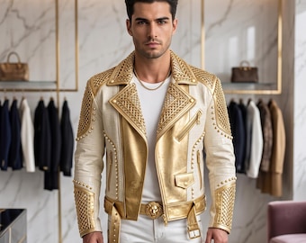 Puede incluir: Una chaqueta de motorista de cuero color crema y oro metalizado con solapas anchas, tachuelas doradas y paneles texturizados de estilo trenzado en hombros y mangas. La chaqueta incluye un cinturón dorado con hebilla de cabeza de león.