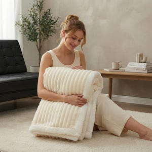 May include: A cream-coloured, rectangular throw blanket featuring a textured, ribbed pattern on one side and a soft, plush sherpa-style fleece lining on the reverse. The blanket is folded, showcasing the contrast between the ribbed fabric and the fuzzy trim.