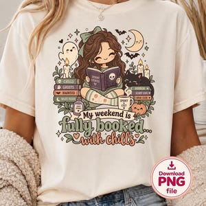 Puede incluir: Una camiseta de color crema con una ilustración gráfica de una persona leyendo un libro titulado Spooky Stories, rodeada de pilas de libros, un fantasma, un gato negro, velas, una calabaza y una taza, con el texto My weekend is fully booked with chills.
