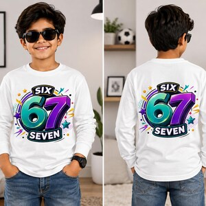 Op de afbeelding: Een wit shirt met lange mouwen en een grafische print op de voor- en achterkant. Het ontwerp toont de tekst SIX 67 SEVEN in grote, dikke, turquoise en paarse 3D-cijfers en zwarte letters, omringd door kleurrijke sterren en stippen.