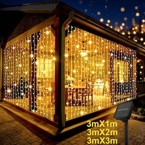 Puede incluir: Una cortina de luces LED de color blanco cálido que cuelga del techo de un patio cubierto. Las luces están dispuestas en hilos verticales. Un panel solar negro sobre una estaca muestra el texto 3mX1m, 3mX2m, 3mX3m.