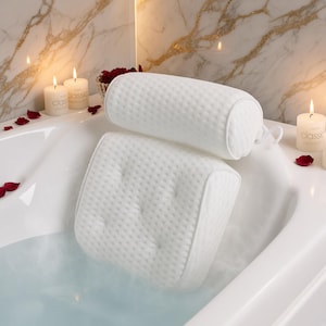 Puede incluir: Una almohada de baño blanca con una superficie texturizada y con hoyuelos, con un diseño de dos partes que consiste en una sección trasera rectangular con hendiduras acolchadas y una sección de reposacabezas cilíndrica, dentro de una bañera.