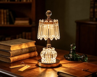 May include: A table lamp featuring a clear, faceted glass shade with a scalloped edge and a matching glass base, supported by a gold-toned metal stem. The lamp emits a warm, glowing light that illuminates the surrounding surface and objects.