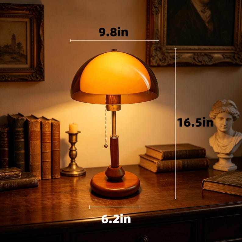 Puede incluir: Una l&aacute;mpara de mesa con pantalla de cristal &aacute;mbar en forma de c&uacute;pula, v&aacute;stago color lat&oacute;n y base redonda de madera. La l&aacute;mpara cuenta con un interruptor de cadena y mide 24,9 cm de ancho, 41,9 cm de alto y 15,7 cm de di&aacute;metro de base.