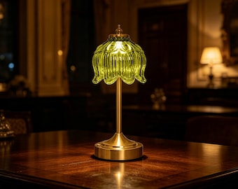 May include: A table lamp featuring a translucent, lime green, fluted glass shade shaped like a flower petal. The lamp has a slender, brushed brass-coloured metal stem and a circular base, emitting a soft, warm glow from within the glass shade.
