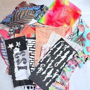 May include: A collection of mixed media art pieces including painted leaves with blue and orange patterns, a bright pink and yellow envelope, and rectangular paper scraps featuring black and white prints, handwritten text, and abstract colorful textures.