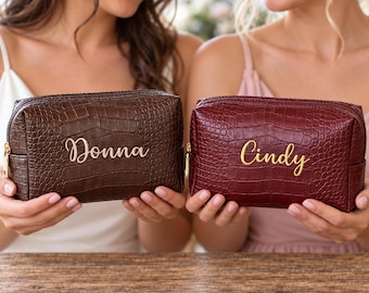 May include: Two rectangular cosmetic bags with a textured crocodile skin pattern. One bag is dark brown with the name Donna in gold script, and the other is deep red with the name Cindy in gold script. Both feature gold metal zippers.