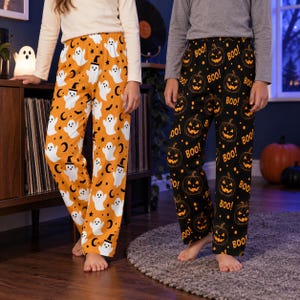 May include: Two pairs of lounge pants. One pair is orange with a white ghost, black witch hat, and crescent moon pattern. The other pair is black with an orange jack-o'-lantern and the word BOO printed in an orange font throughout the fabric.