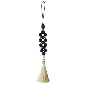 May include: A decorative hanging ornament featuring a vertical arrangement of dark brown spherical beads interspersed with small silver-toned accents. The ornament is suspended by a black cord and finished with a long, cream-coloured fabric tassel.