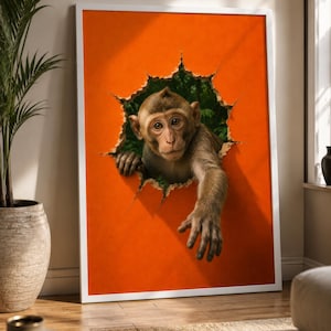 Op de afbeelding: Een ingelijste kunstdruk met een realistische aap die door een grillig, rond gat in een feloranje oppervlak kijkt. De aap heeft bruine vacht, grote donkere ogen en één arm naar voren gestrekt alsof hij uit de jungle-achtergrond reikt.
