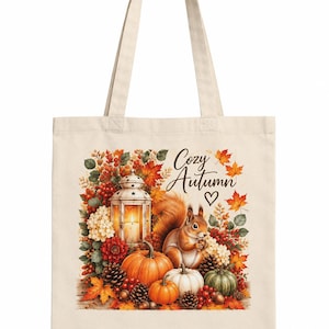 Op de afbeelding: Een beige canvas tas met een bedrukte illustratie van een eekhoorn, pompoenen, dennenappels, bessen en een verlichte lantaarn. De tekst "Cozy Autumn" staat in een sierlijk lettertype boven de eekhoorn, vergezeld door een klein hartje.