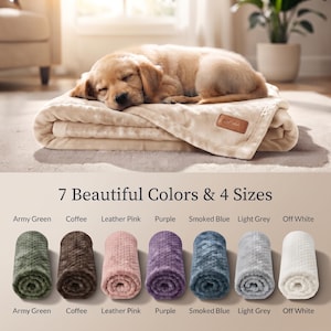 Peut inclure: Une couverture texturée beige clair avec une petite étiquette rectangulaire marron, sur laquelle repose un chiot doré endormi. En dessous, le texte indique 7 Beautiful Colors & 4 Sizes, montrant sept couvertures roulées en vert armée, café, rose cuir, violet, bleu fumé, gris clair et blanc cassé.
