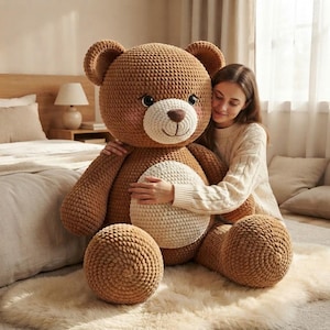 Puede incluir: Un oso de peluche grande, tejido a ganchillo en color marrón, con un hocico color crema y un parche circular color crema en la barriga. El oso presenta ojos oscuros, una nariz marrón bordada y una boca sencilla, hecho de hilo grueso y texturizado.