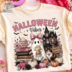 Könnte beinhalten: Ein cremefarbenes T-Shirt mit einem Aufdruck, der den Text HALLOWEEN VIBES, ein Gespenst mit rosa Schleife, ein Spukhaus, eine Glückskatze und Bücherstapel mit den Titeln Witches Brew, Spellbinding Secrets, Potion Recipes, Midnight Lore und Forbidden Brews zeigt.