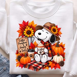 Könnte beinhalten: Ein weißes Sweatshirt mit einer Grafik eines weißen Zeichentrickhundes, der einen braunen Hut und einen karierten Schal trägt und eine Kaffeetasse hält. Das Design zeigt orangefarbene Kürbisse, Sonnenblumen, rote Beeren, Tannenzapfen und ein Schild mit der Aufschrift Coffee Pumpkins & Happy Tails.