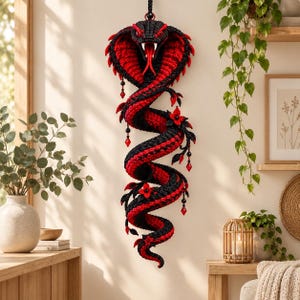 May include: A wall-hanging crochet cobra sculpture featuring a coiled body in alternating black and red yarn. The snake has a flared hood, a wide-open mouth with a red forked tongue, and is decorated with small black beads and red crystal-like accents.
