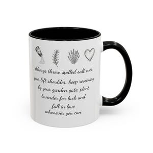 Puede incluir: Una taza de cerámica blanca con asa y borde negros. La taza presenta ilustraciones de línea negra de un salero, una ramita de romero, un ramo de lavanda y un corazón, con el texto: Always throw spilled salt over your left shoulder, keep rosemary by your garden gate, plant lavender for luck and fall in love whenever you can.