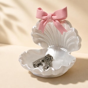 Portagioie a forma di conchiglia con fiocco rosa.