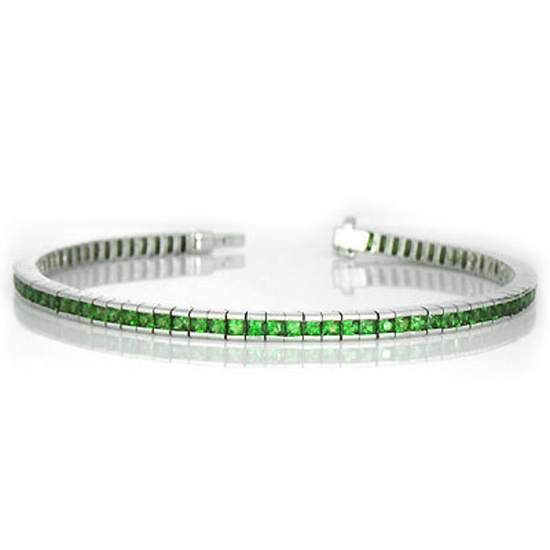 Puede incluir: Un brazalete de tenis de plata con una fila de piedras preciosas cuadradas verdes.