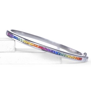 Op de afbeelding: Een zilveren armband met een regenboog van edelstenen in een enkele rij rond de band.