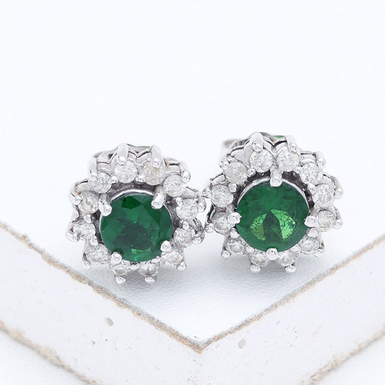 May include: A pair of silver earrings with a green gemstone surrounded by smaller white gemstones.