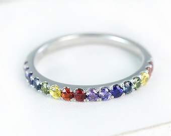 May include: A silver band ring with a rainbow of gemstones. The ring is set with sapphires, peridot, citrine, garnet, amethyst, and blue topaz.