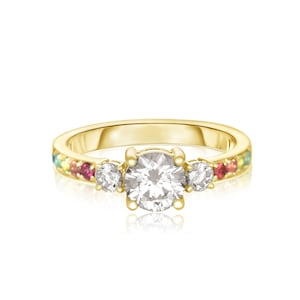 Puede incluir: Un anillo de oro con un gran diamante redondo central y dos diamantes más pequeños a cada lado. La banda está engastada con una fila de piedras preciosas de colores.